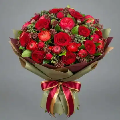 A lush rose and ranunculus bouquet with deep crimson petals and soft greenery in a professional studio setting.