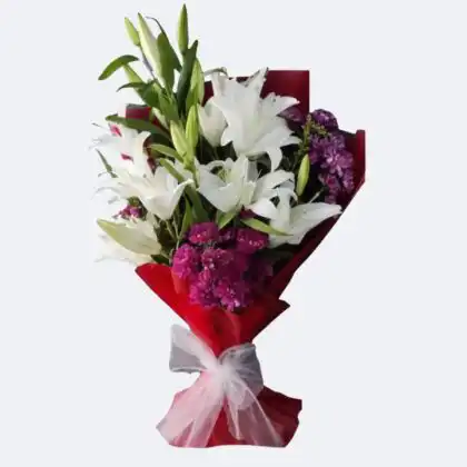 A hand holding a fresh white lily flower bouquet elegantly wrapped in royal purple paper.
