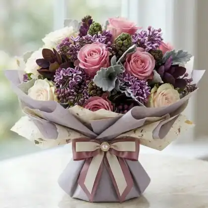 Handcrafted roses and lilac bouquet arranged in a stylish vase with soft green foliage.