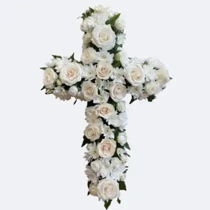 A handcrafted funeral cross flowers arrangement featuring fresh white roses and chrysanthemums on a woven background.