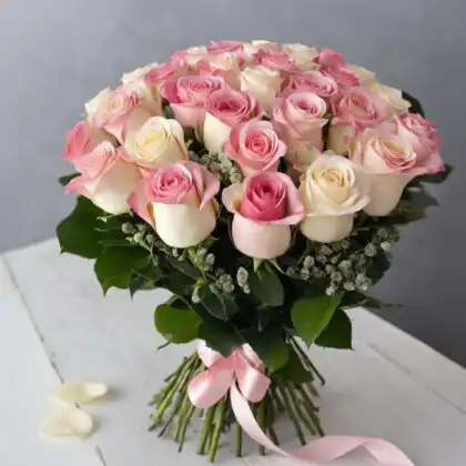 A romantic beautiful pink rose bouquet featuring fresh cream roses and delicate white baby's breath blossoms on a wooden surface.