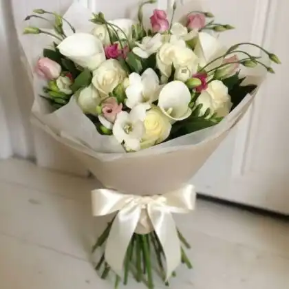 A handcrafted calla lilies and white roses bouquet elegantly wrapped in craft paper with a silk ribbon.
