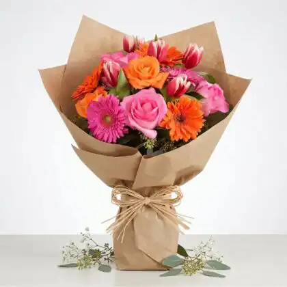 A vibrant tulip and gerbera daisy bouquet arranged with fresh greenery in a clean studio setting.